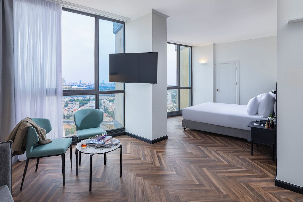 A modern hotel room with a large window, a bed, a TV, a desk, and a chair.