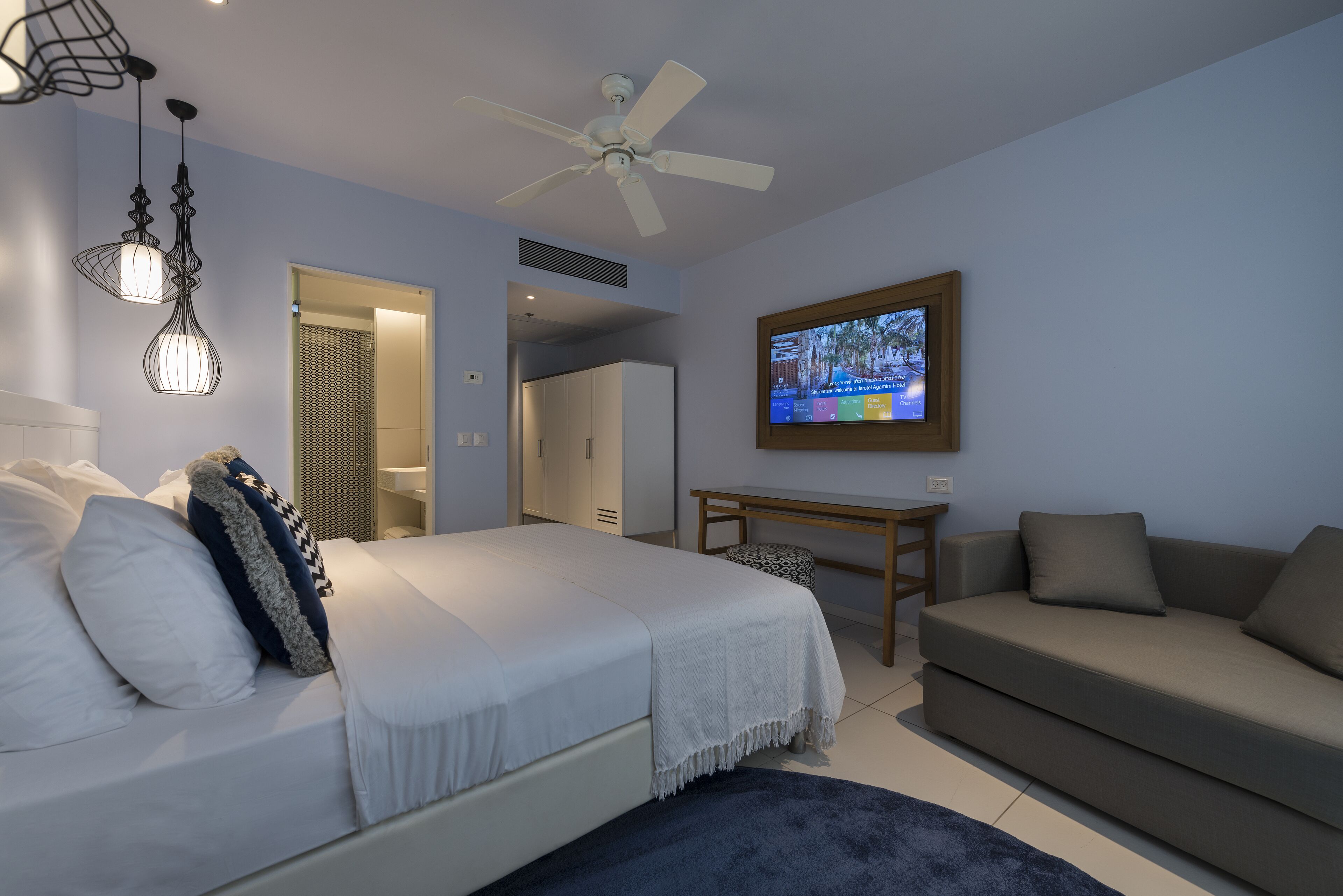 A bedroom with a bed, a ceiling fan, a TV, a sofa, and a desk.