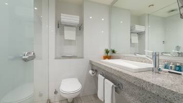 A modern bathroom with a glass shower enclosure, a white toilet, a sink with a granite countertop, and a mirror above the sink.