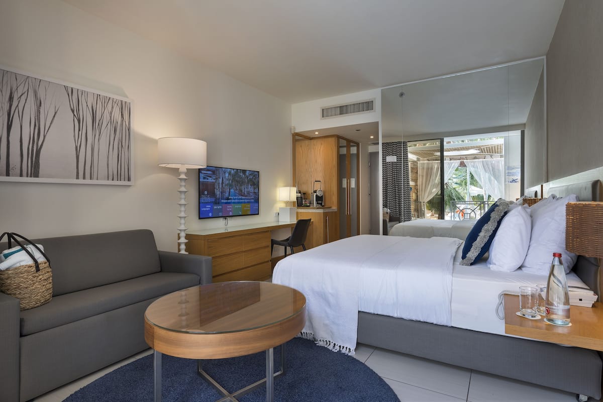 A modern hotel room with a bed, a sofa, a desk, and a TV.