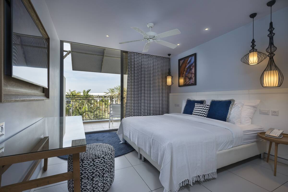 A modern bedroom with a large bed, a ceiling fan, and a balcony with a view.