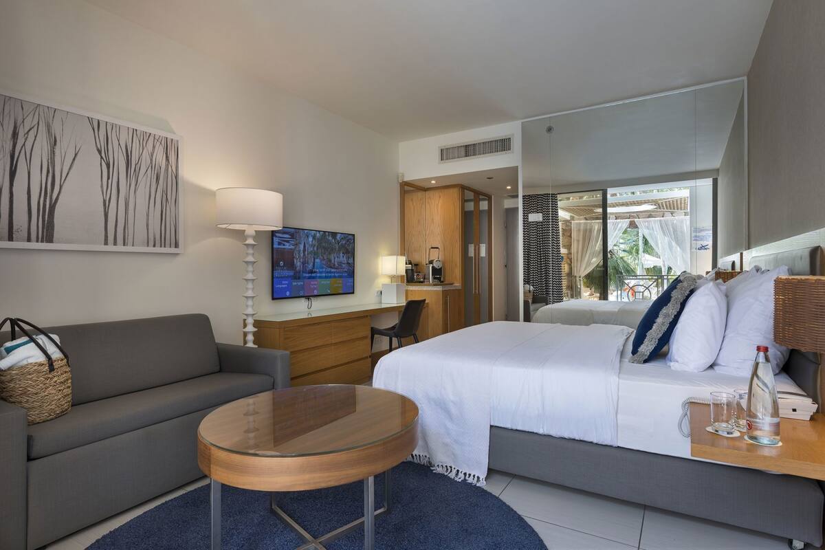 A hotel room with a bed, a desk, a chair, a sofa, a TV, and a window with a view.