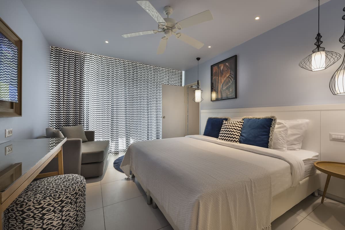 A modern bedroom with a bed, a desk, a chair, and a ceiling fan.