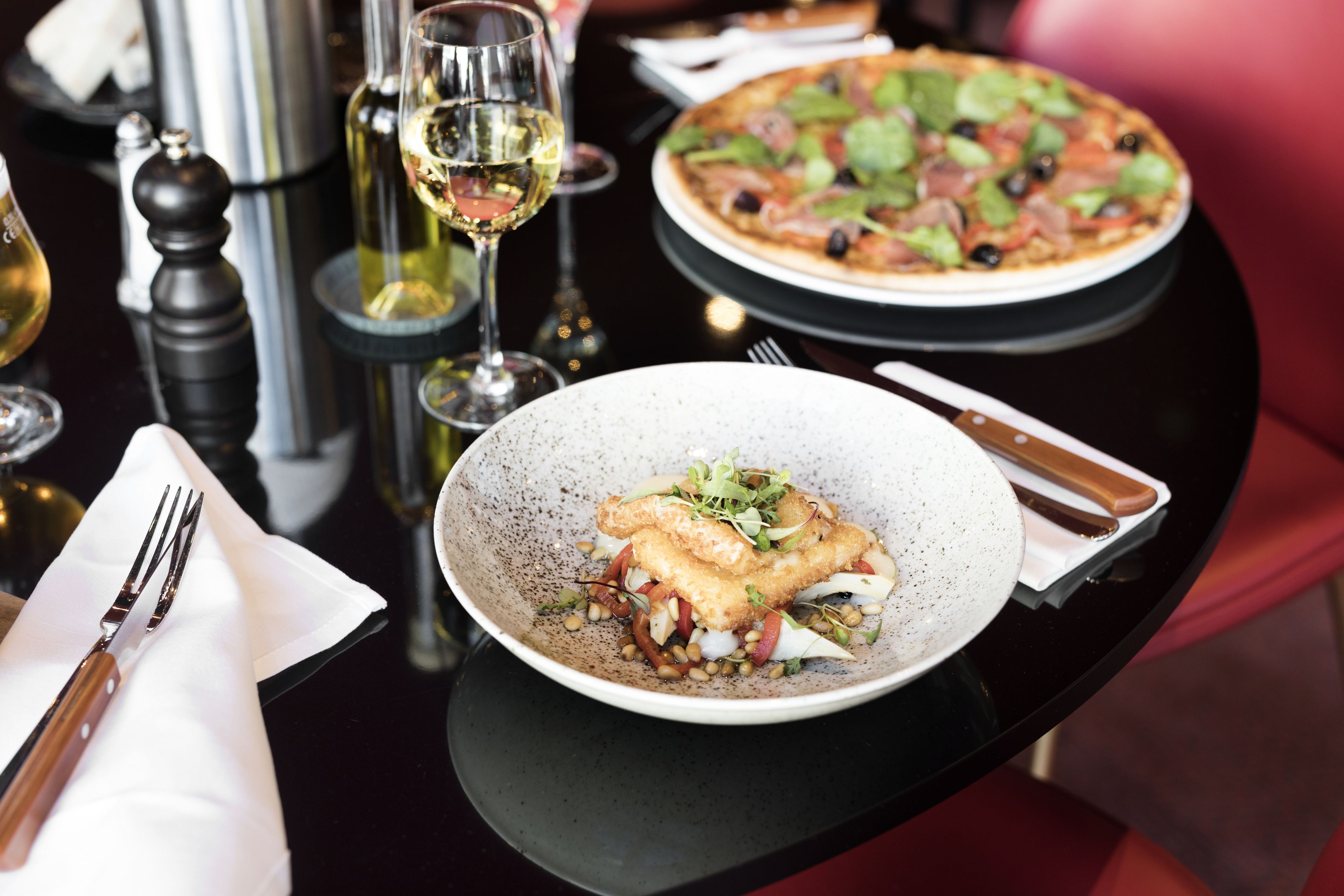 A dining table with a plate of food, a glass of wine, and a pizza.