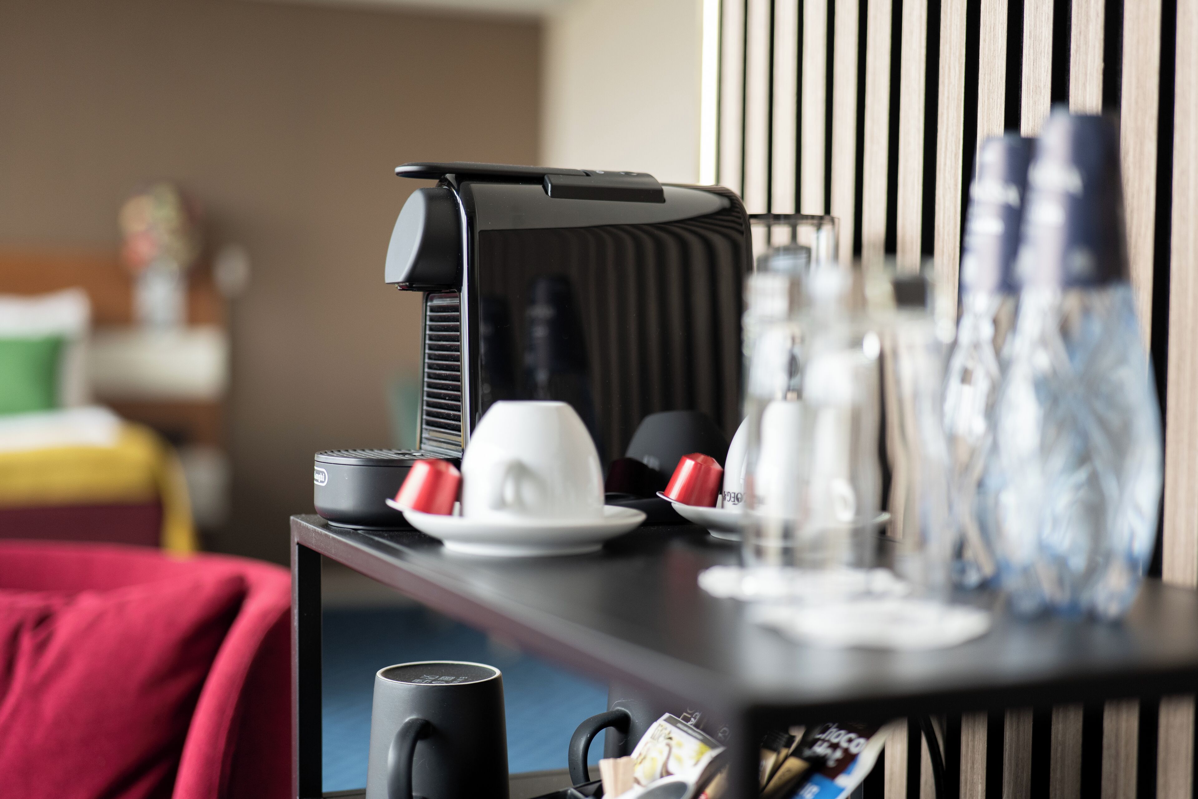 Une chambre d’hôtel avec un lit, un bureau, une machine à café, des tasses et une bouteille d’eau.