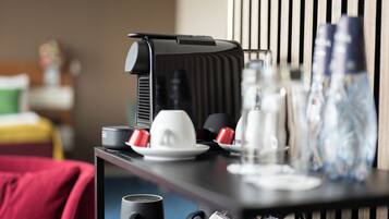 A hotel room with a bed, a desk with a coffee maker, cups, and a water bottle.
