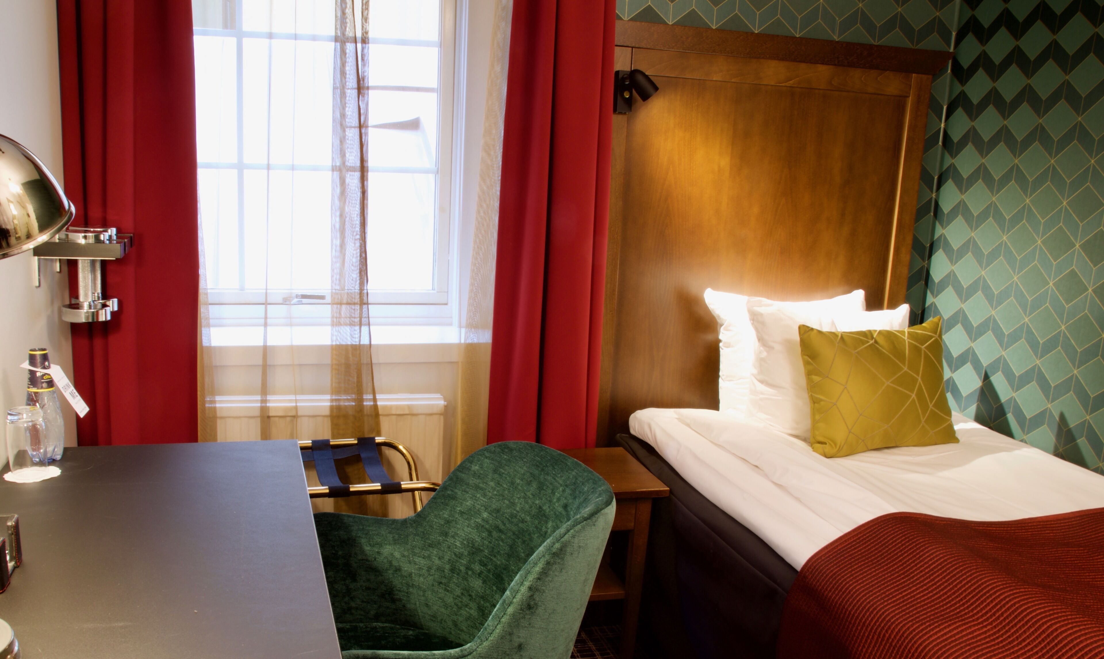 Una habitación de hotel con una cama, un escritorio, una silla y una ventana con cortinas.