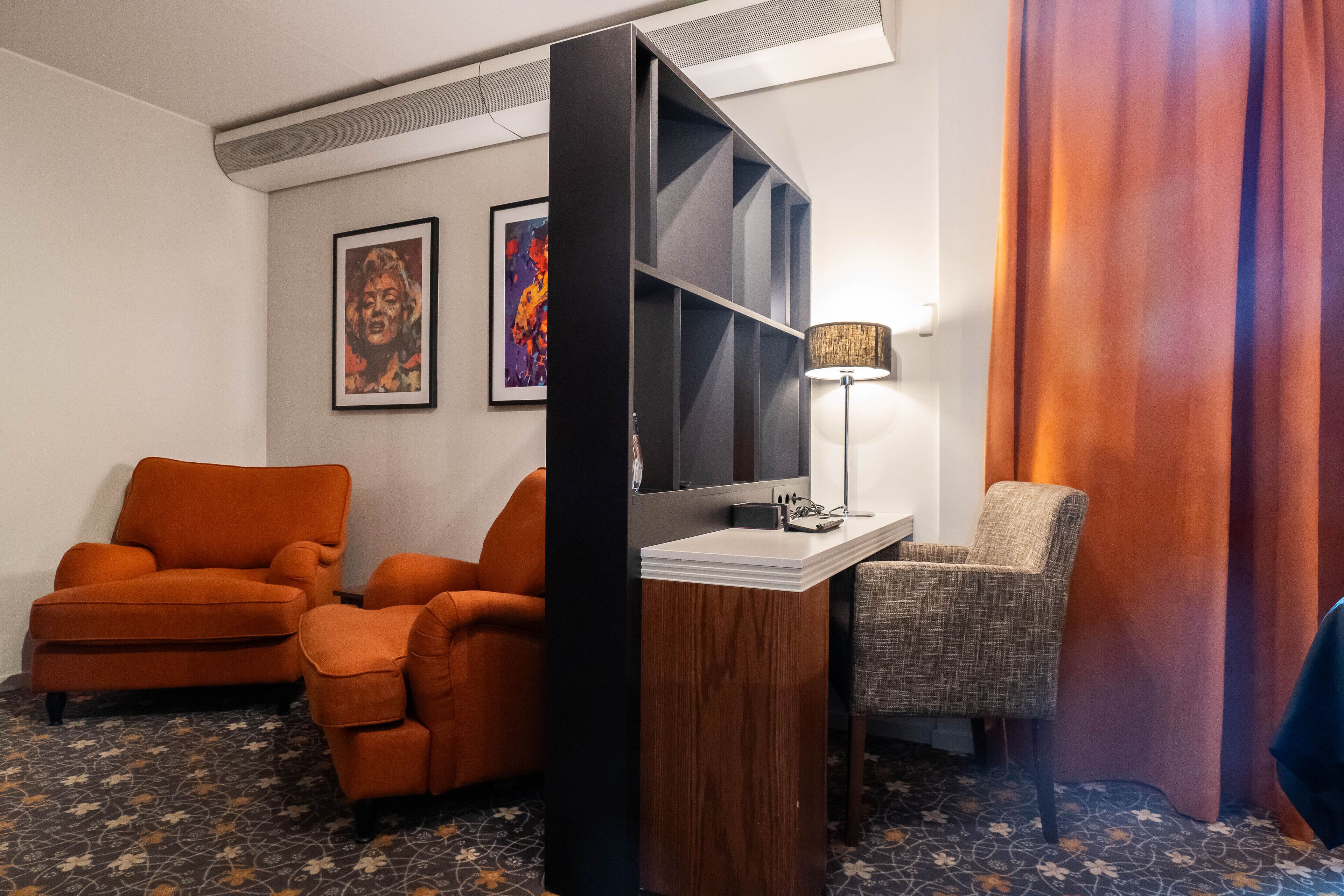 Una habitación con dos sillones naranjas, una mesita de madera, una lámpara y un ventanal con vistas.