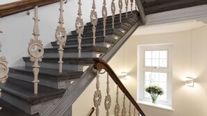 Un escalier orné de balustres blancs et de marches sombres, menant à un palier agrémenté d’une fenêtre et d’un vase de fleurs.