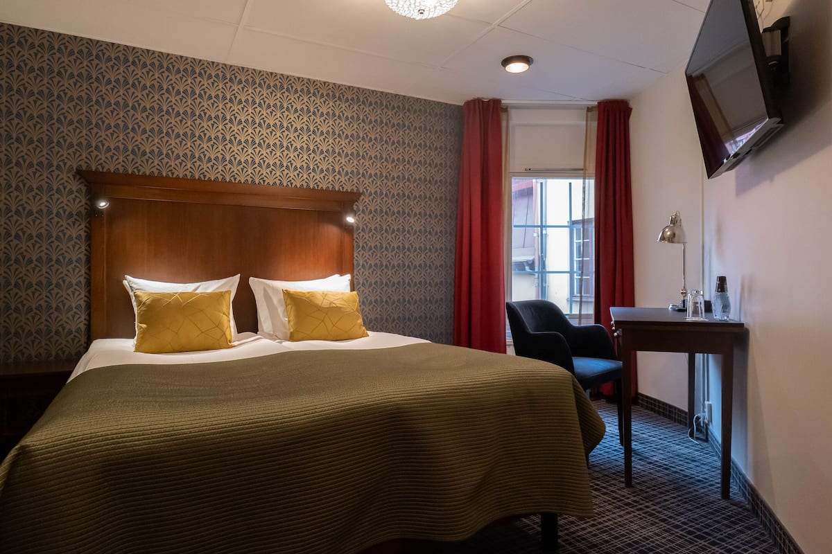 A hotel room with a large bed, a desk, a chair, and a television on the wall.