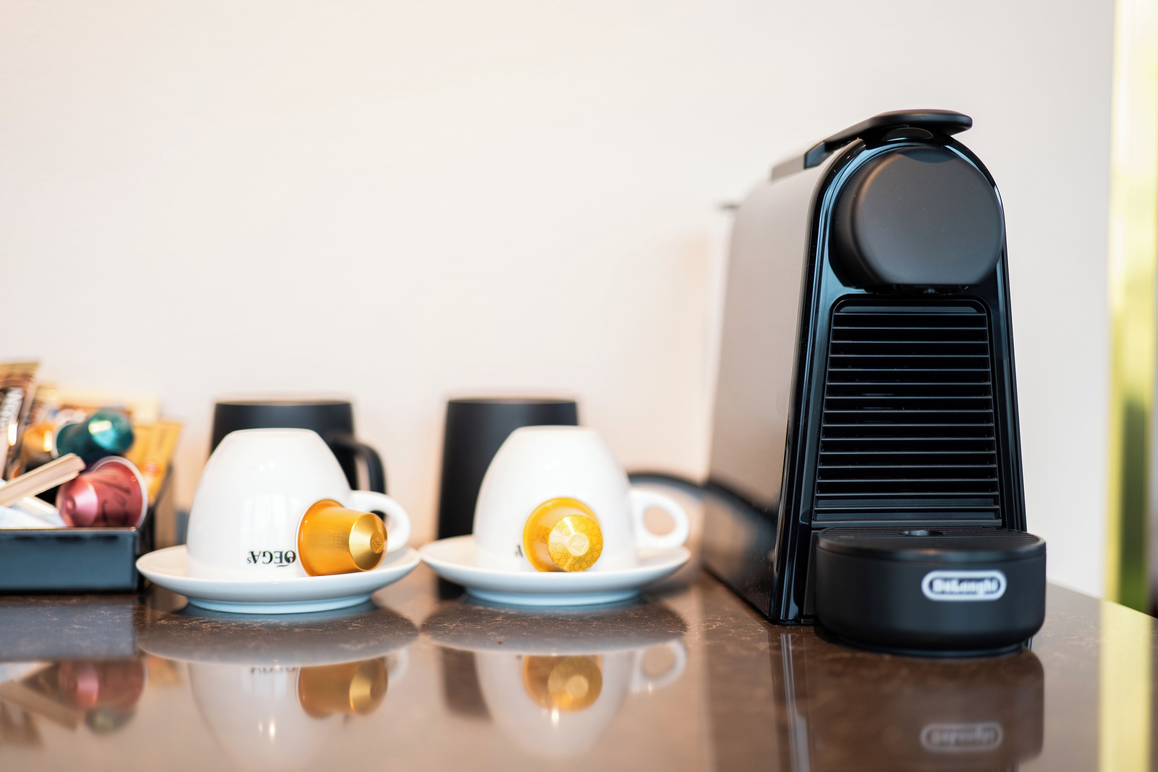 A table with two white cups, one with a yellow object, and a black device with a logo.