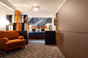 Habitación de hotel con cama, sofá, alfombra estampada y un cuadro abstracto grande en la pared.
