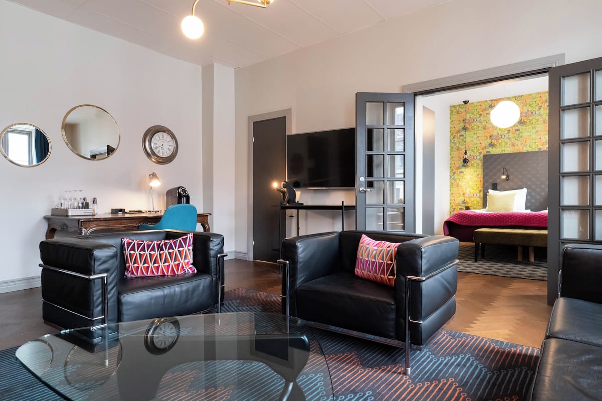 A modern living room with a glass coffee table, black leather sofas, and a flat-screen TV mounted on the wall.
