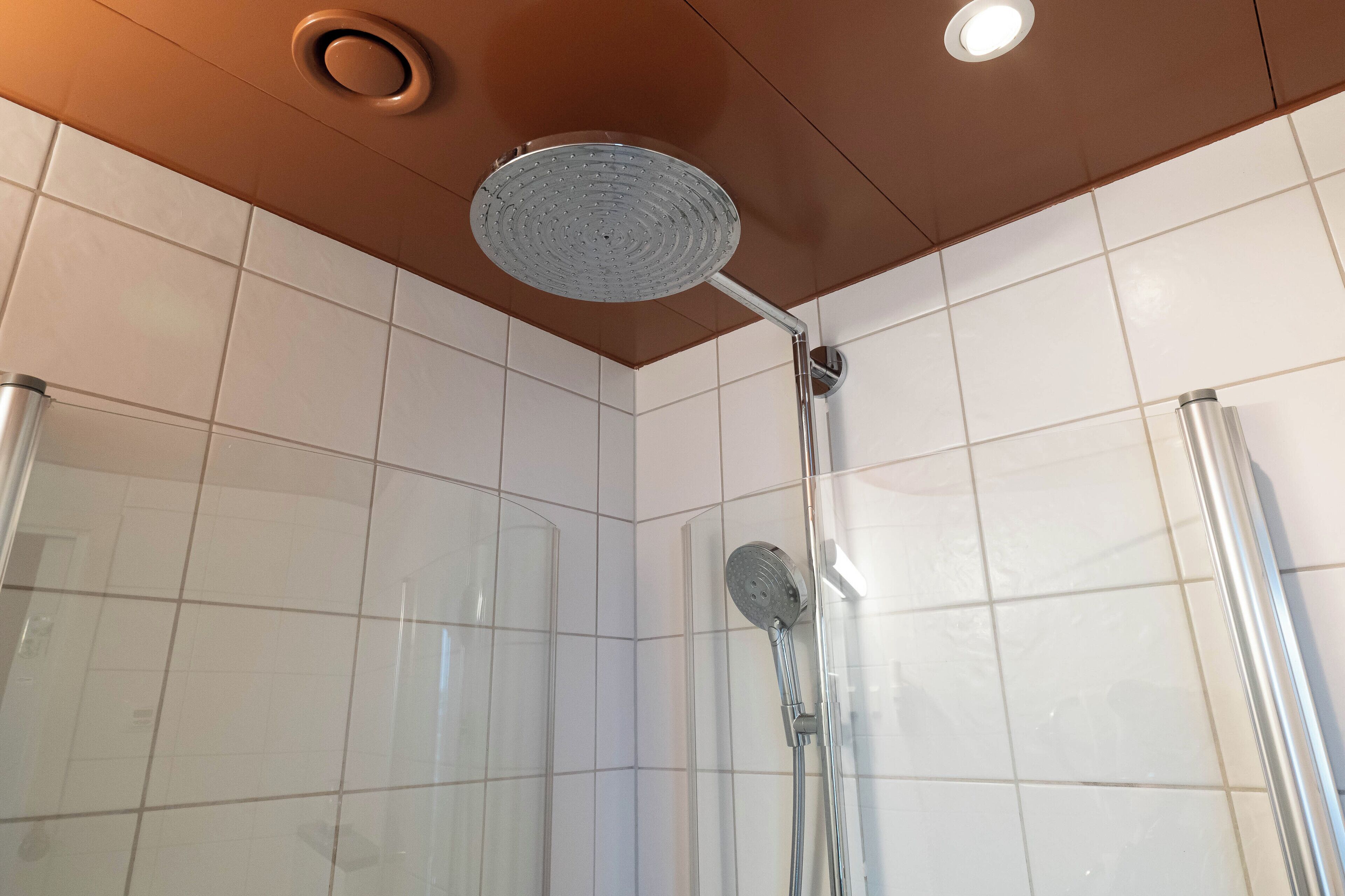 A shower with a handheld showerhead and a wall-mounted faucet in a tiled room.