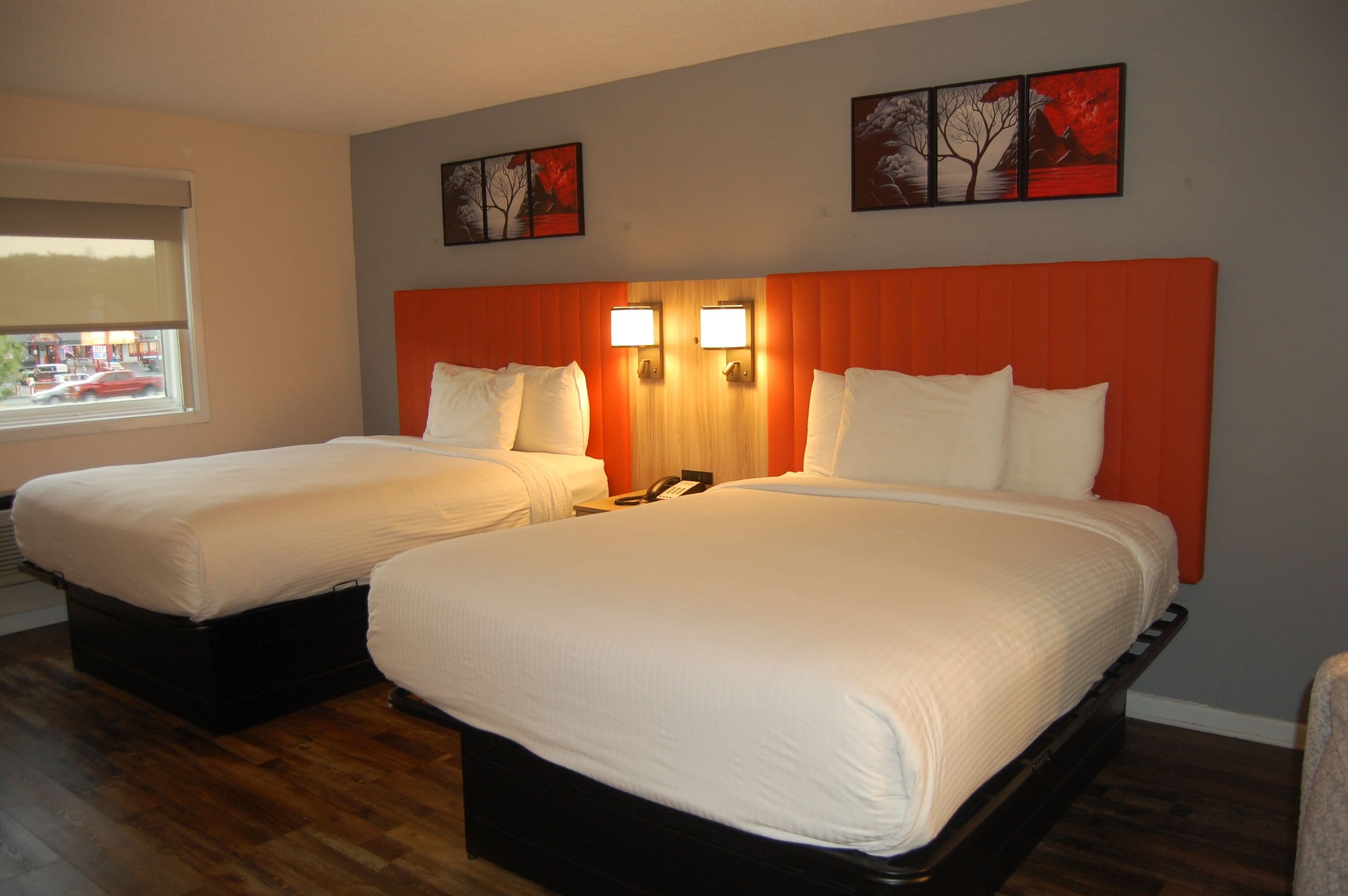Two single beds with wooden headboards and white bedding, a window with a view of a street, and two wall-mounted light fixtures.