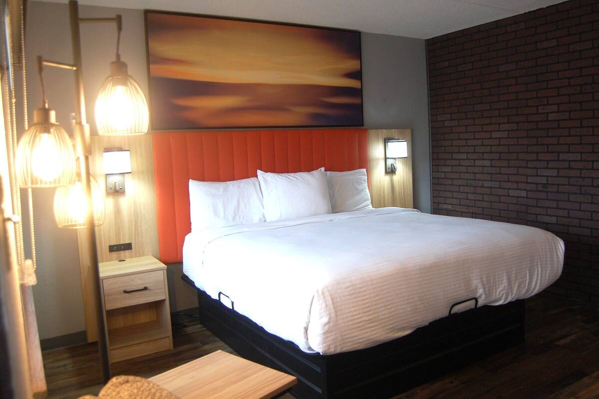 A hotel room with a bed, bedside lamps, a nightstand, and a wooden bench.