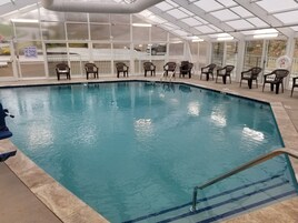 Una piscina interior con agua cristalina, rodeada de sillas y un cartel que indica zona poco profunda y prohibido bucear.