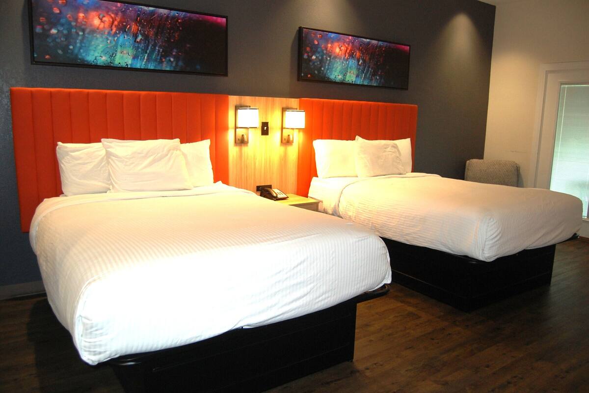 A hotel room with two beds, a wooden floor, and two wall-mounted lamps.