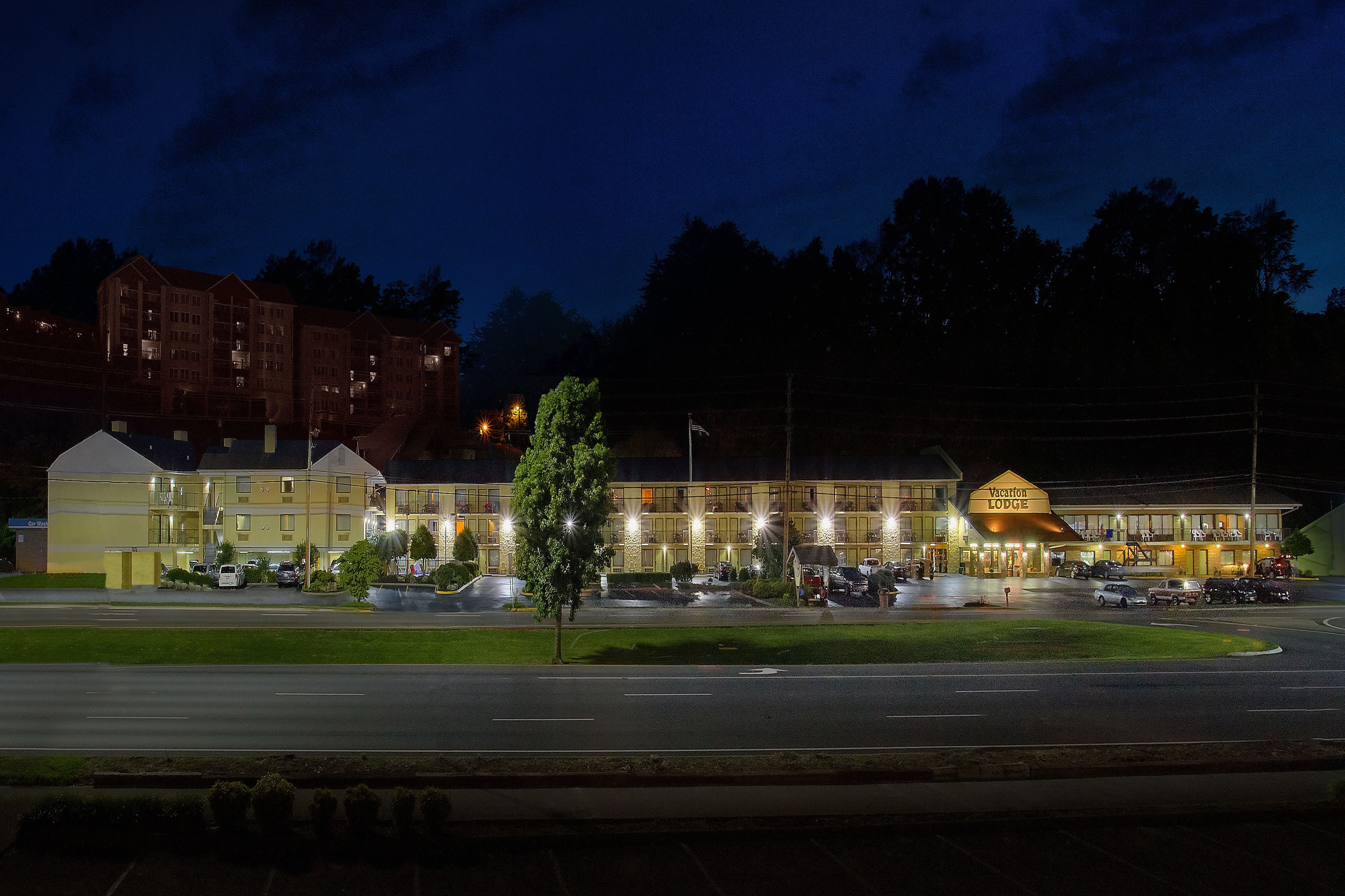 Een meerlaags hotel met een opvallend 'Vacation Lodge' bord, een parkeerplaats met verschillende auto's en een verlichte straat 's nachts.