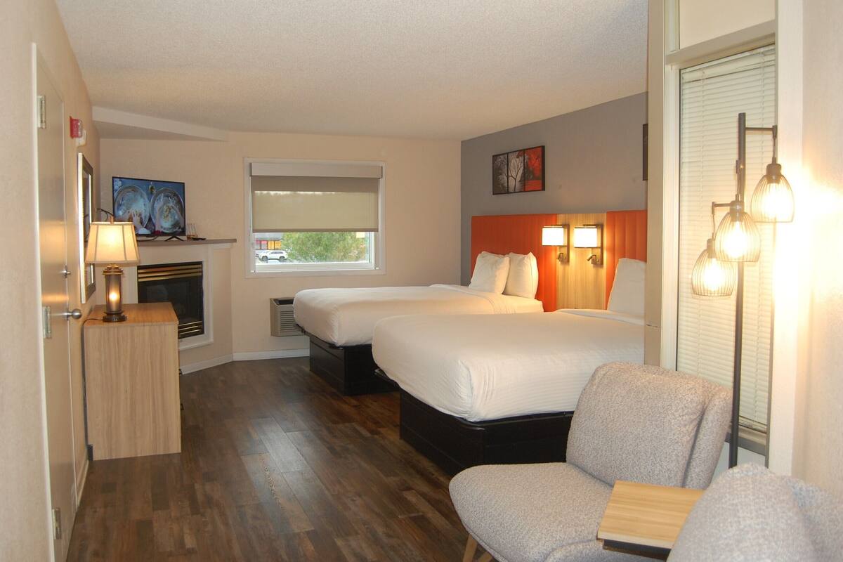 A hotel room with two beds, a sofa, a desk, a lamp, and a window with blinds.