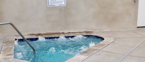 A small hot tub with a metal ladder, surrounded by a concrete deck.