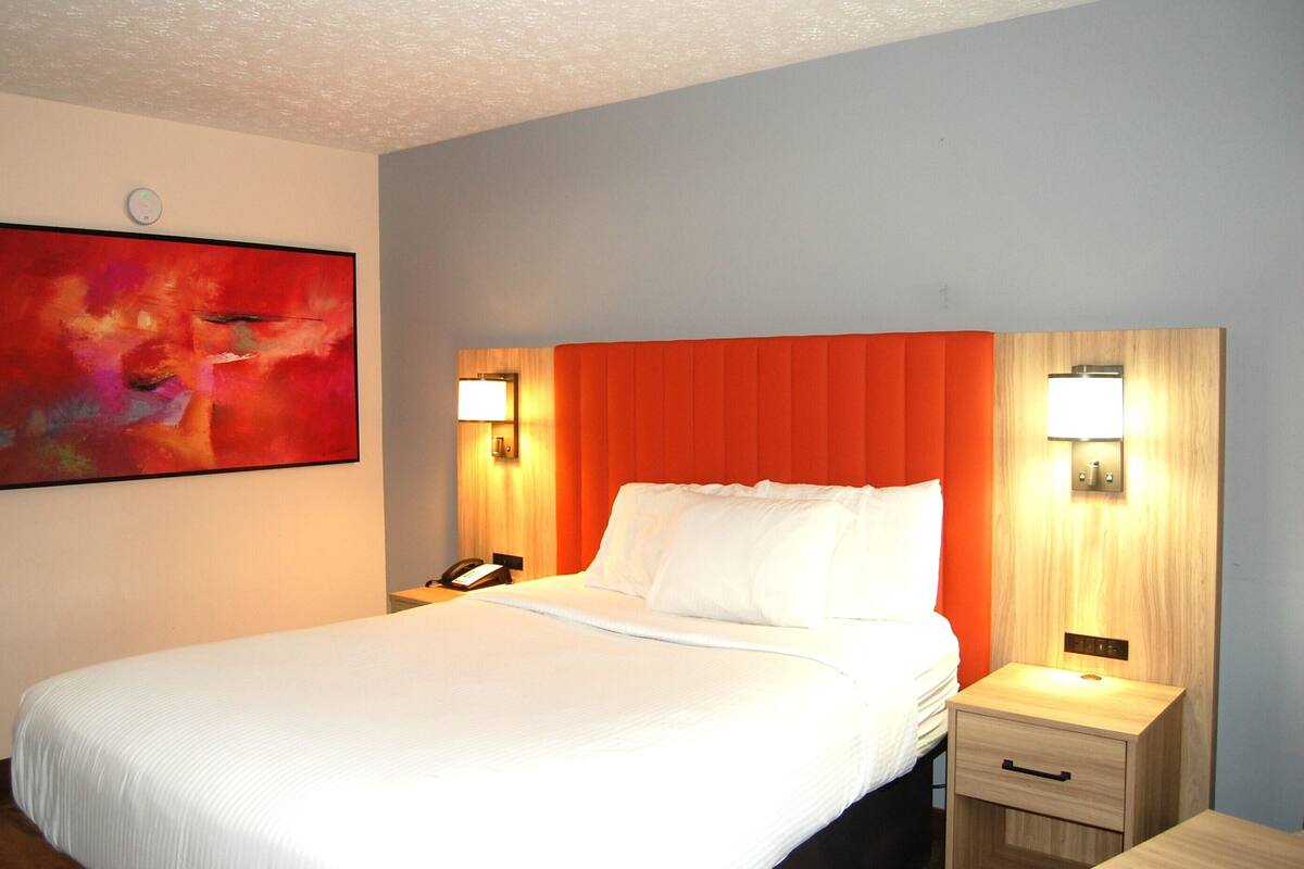 A hotel room with a large bed, two bedside tables with lamps, a painting on the wall, and a wooden headboard.