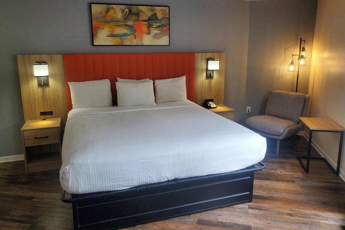A hotel room with a large bed, two bedside tables with lamps, a chair, and a painting on the wall.