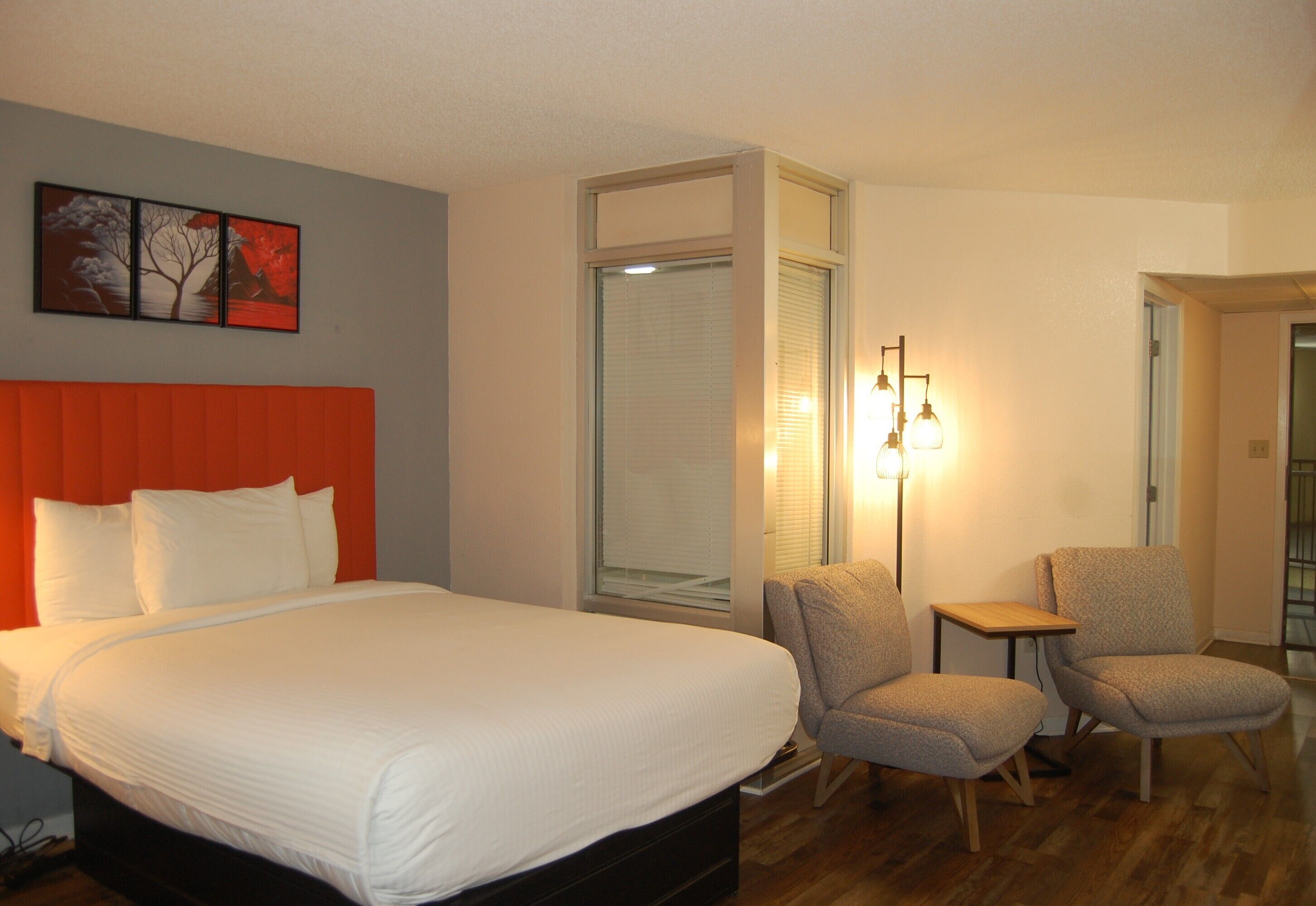 Une chambre d’hôtel avec un grand lit, deux fauteuils, une petite table et un luminaire fixé au mur.