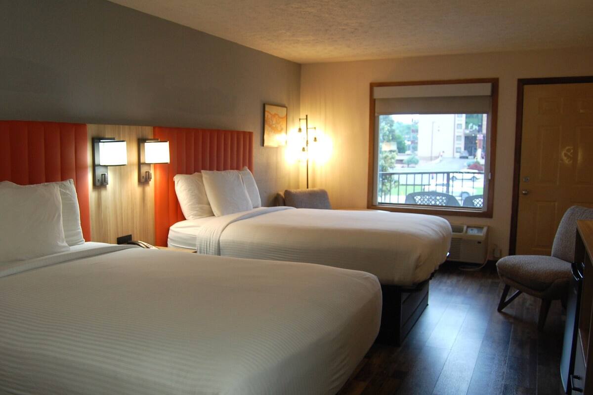 A hotel room with two beds, a chair, a window with a view, and a door.