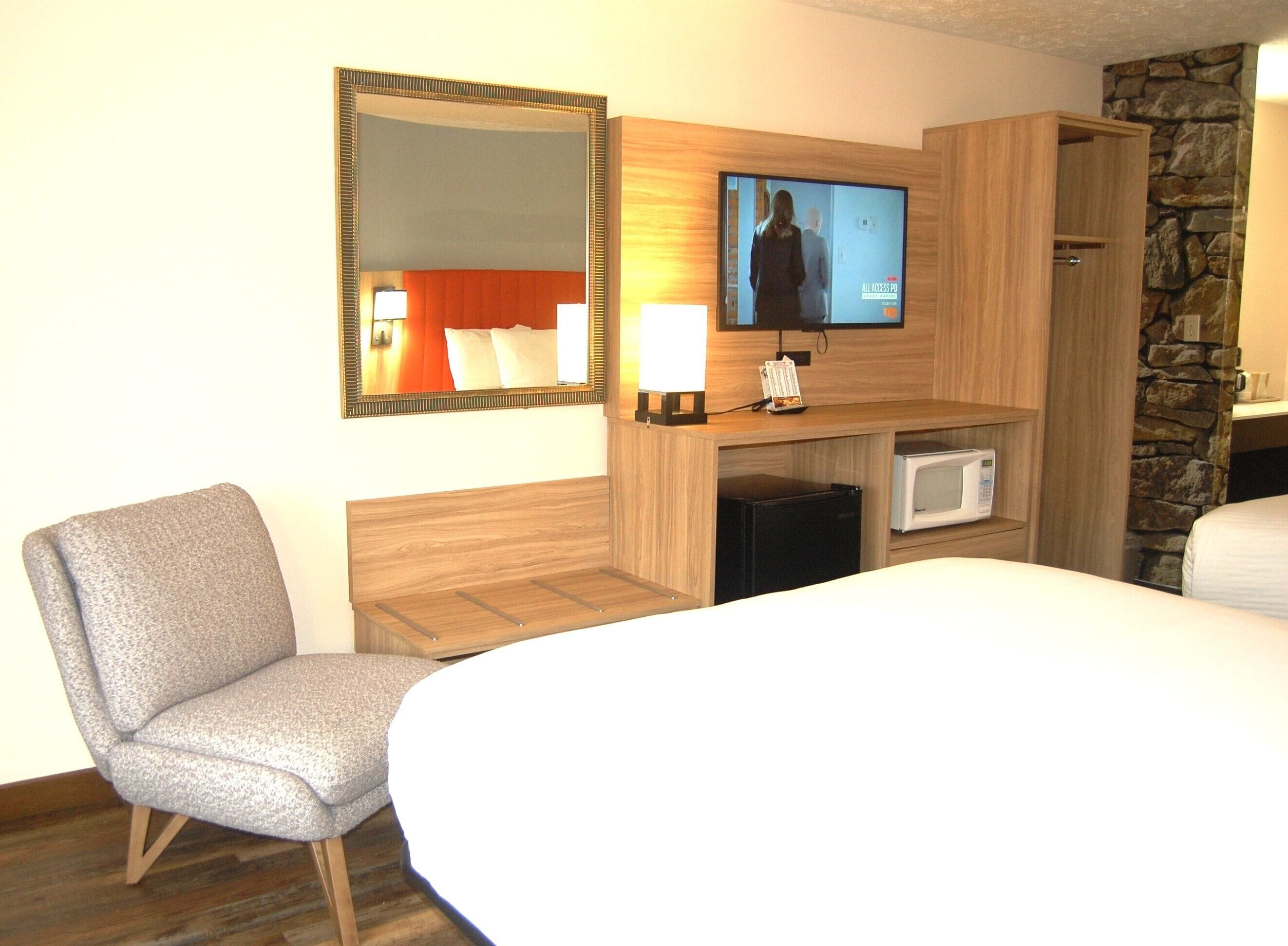 Habitación de hotel con cama, una silla, televisor, microondas y pared de piedra.