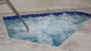Una bañera de hidromasaje con una escalera de metal, rodeada de paredes y suelo de azulejos.