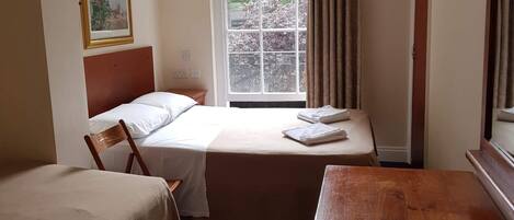 A hotel room with two beds, a wooden desk, a window with curtains, a framed picture on the wall, and a sign thanking guests.