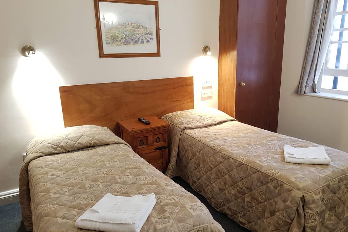 A hotel room with two beds, a wooden headboard, a nightstand with a remote control, and a painting on the wall.