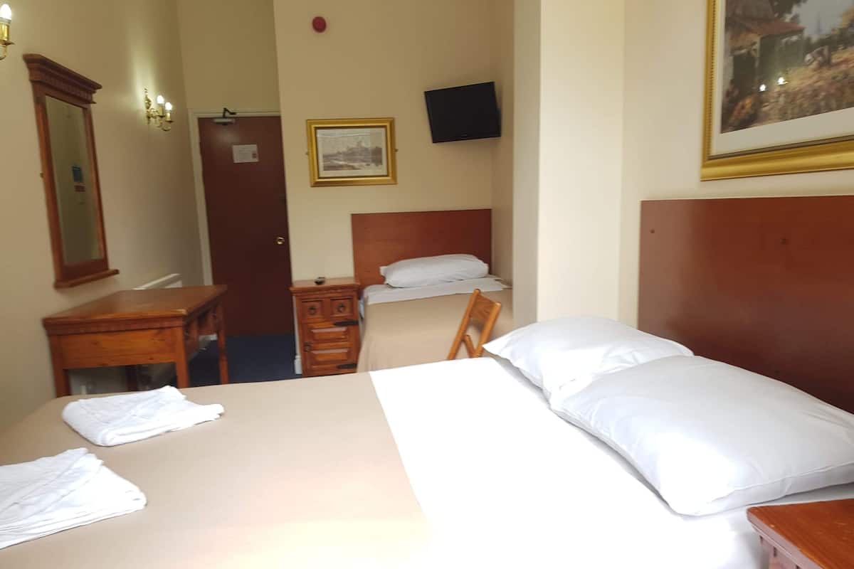 A hotel room with a large bed, a smaller bed, a desk, a chair, a dresser, a TV on the wall, and a framed picture.