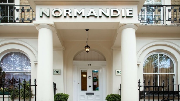 The entrance to Normandie hotel with a white facade, arched windows, and a sign above the door. - Normandie Hotel (London)