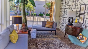 A modern living room with a grey sofa, a patterned rug, a large green plant, and a wall with a geometric design. - Holiday Shores (Myrtle Beach)
