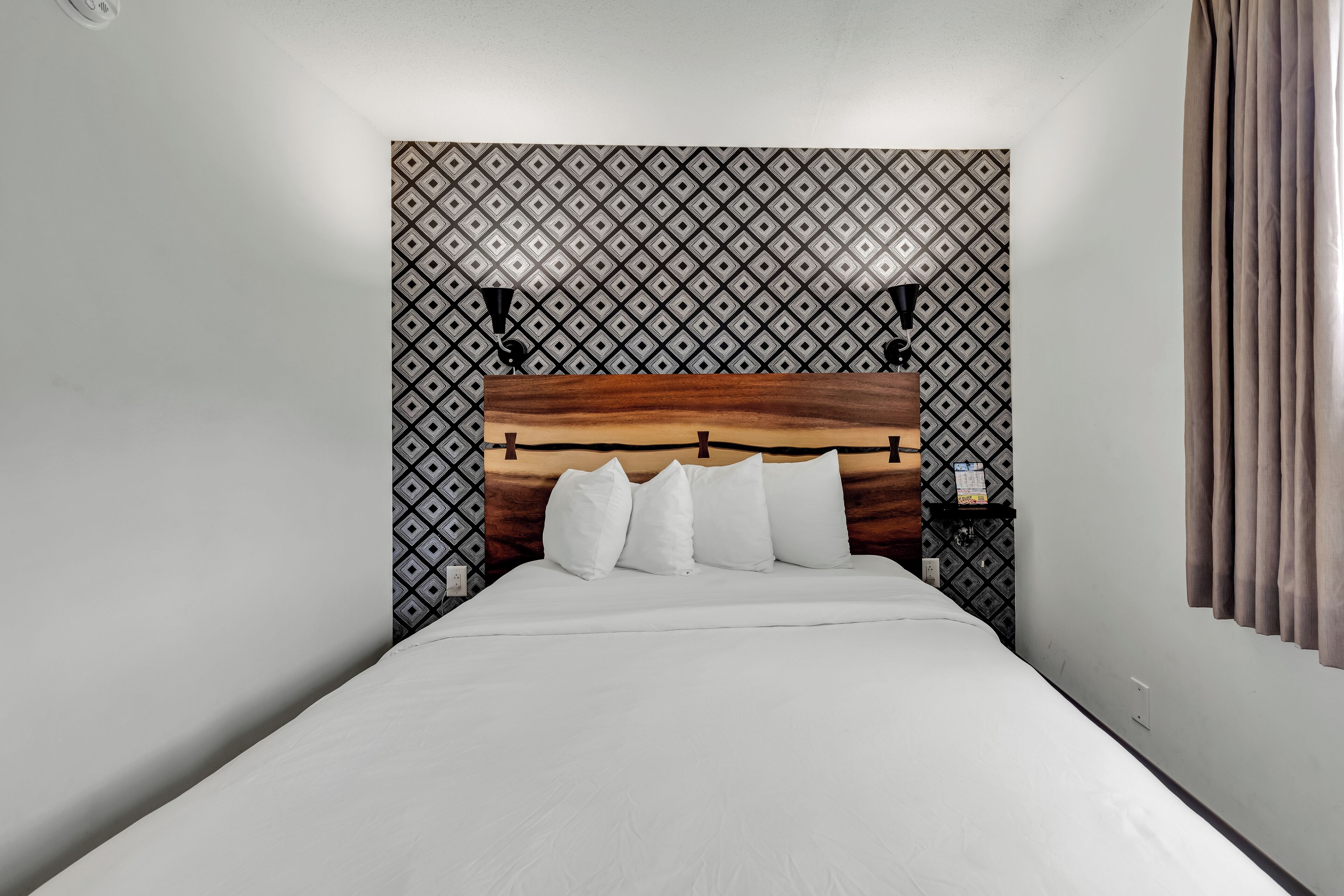 Una cama bien hecha con cabecera de madera, ropa de cama blanca y un papel tapiz estampado en la pared.