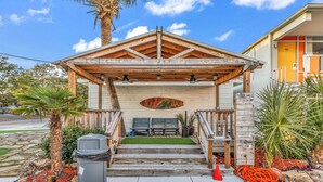 A covered outdoor seating area with a wooden pergola, a bench, and a small garden with palm trees and plants. - Holiday Shores (Myrtle Beach)
