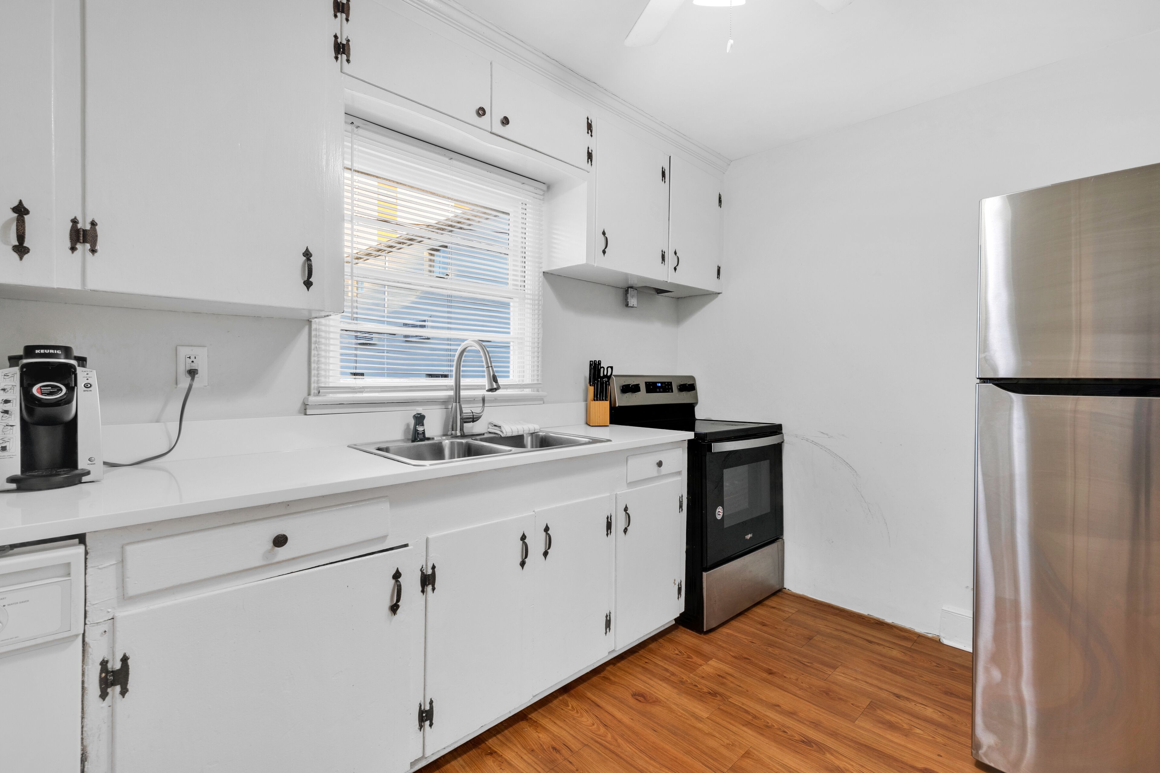 Una cocina moderna con armarios blancos, un refrigerador de acero inoxidable, un horno empotrado y una ventana con persianas.