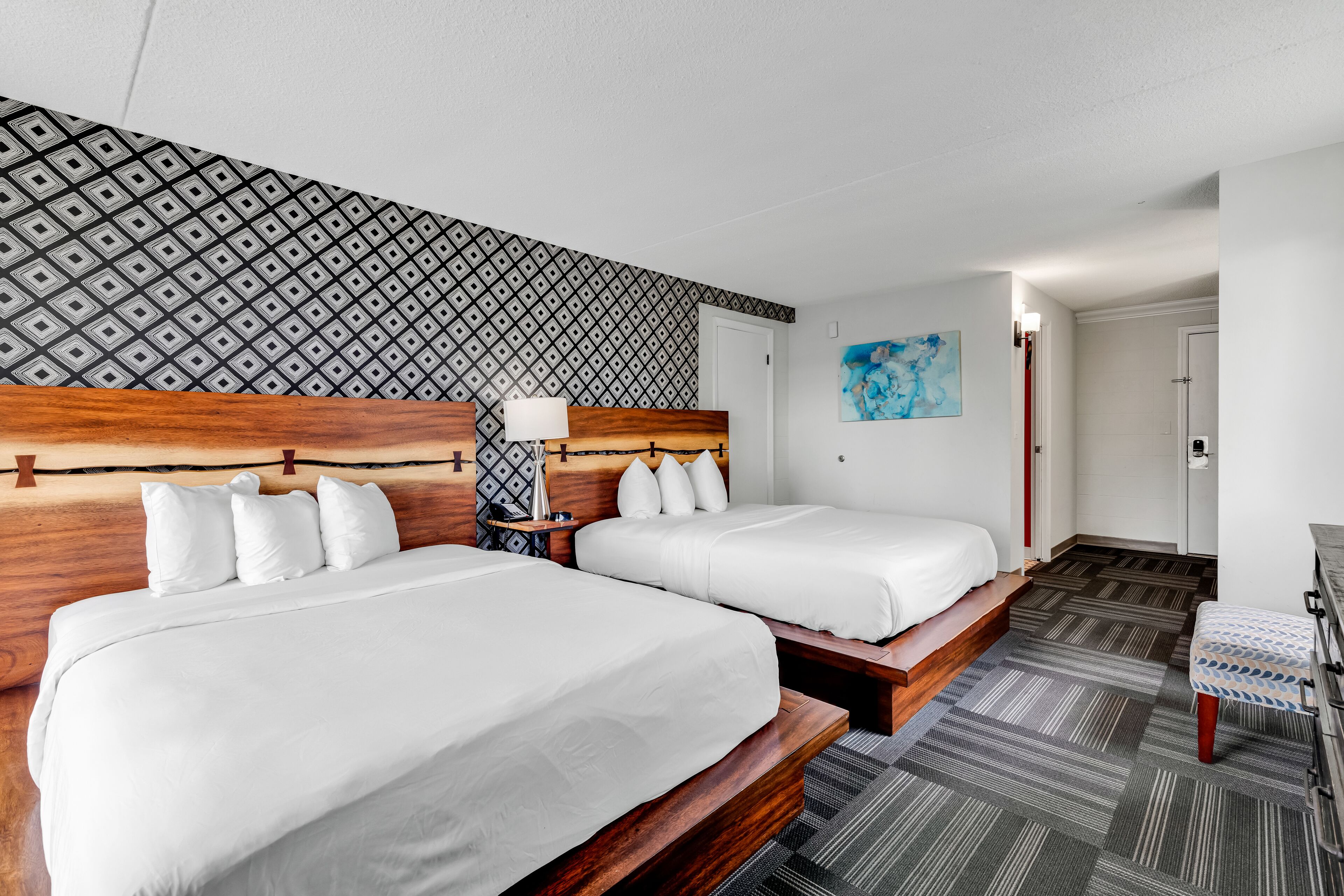 Ett hotellrum med två sängar, en vägg med ett mönster och ett blått konstverk.