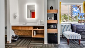 A modern bathroom with a white sink, mirror, and wooden vanity. There is a black refrigerator, a microwave, and a chair with a patterned cushion. - Holiday Shores (Myrtle Beach)
