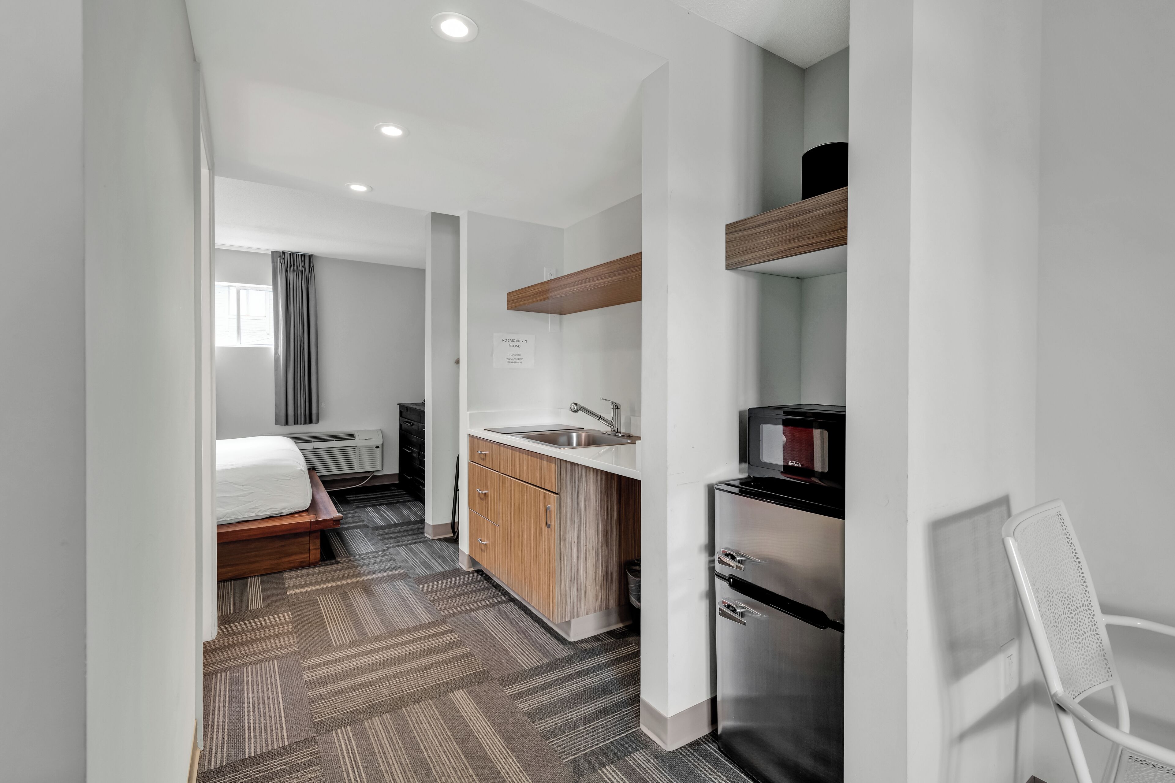 A modern hotel room with a bed, a kitchenette, and a bathroom.