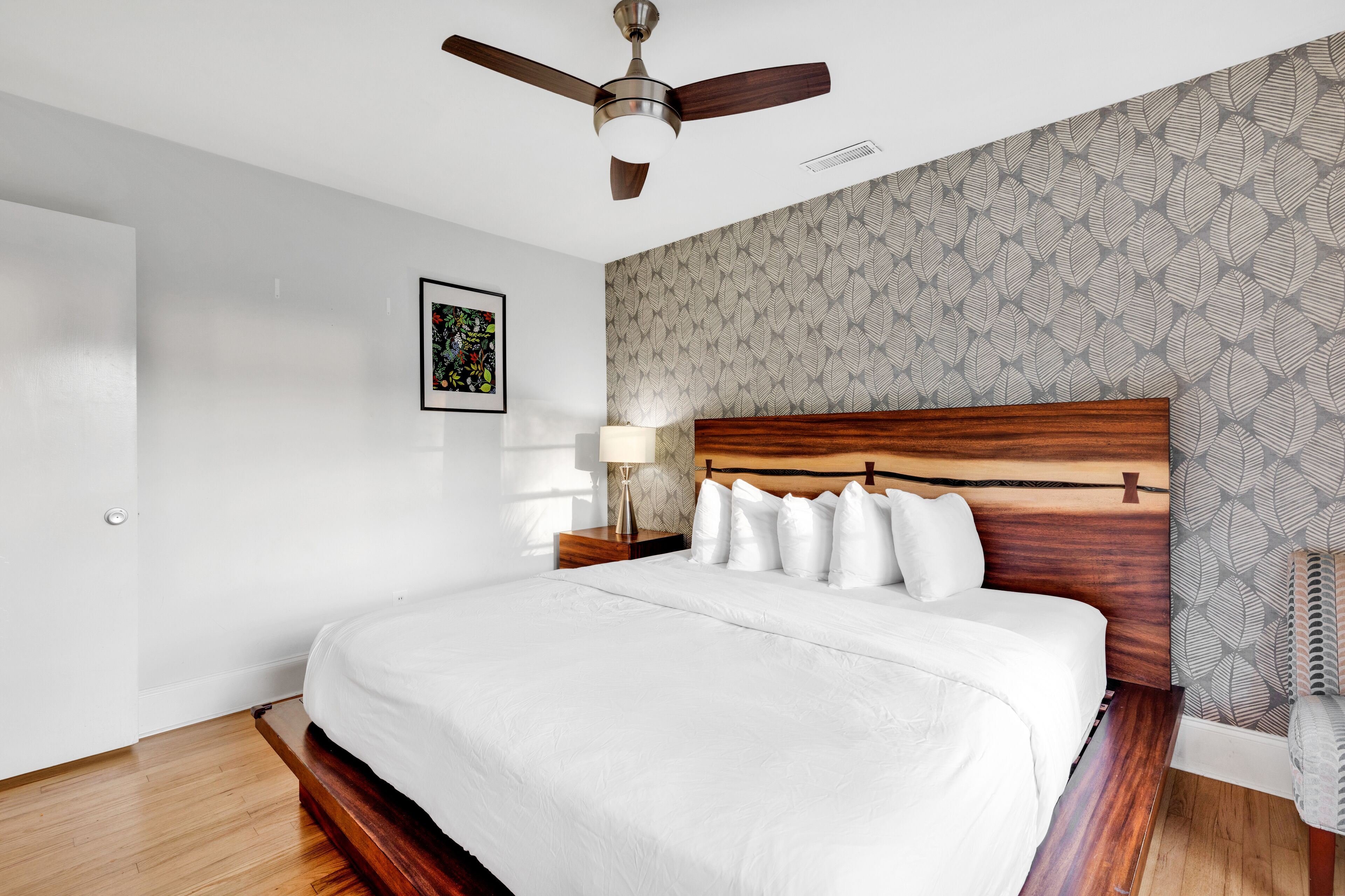 A neatly made bed with white bedding, a wooden headboard, and a ceiling fan.