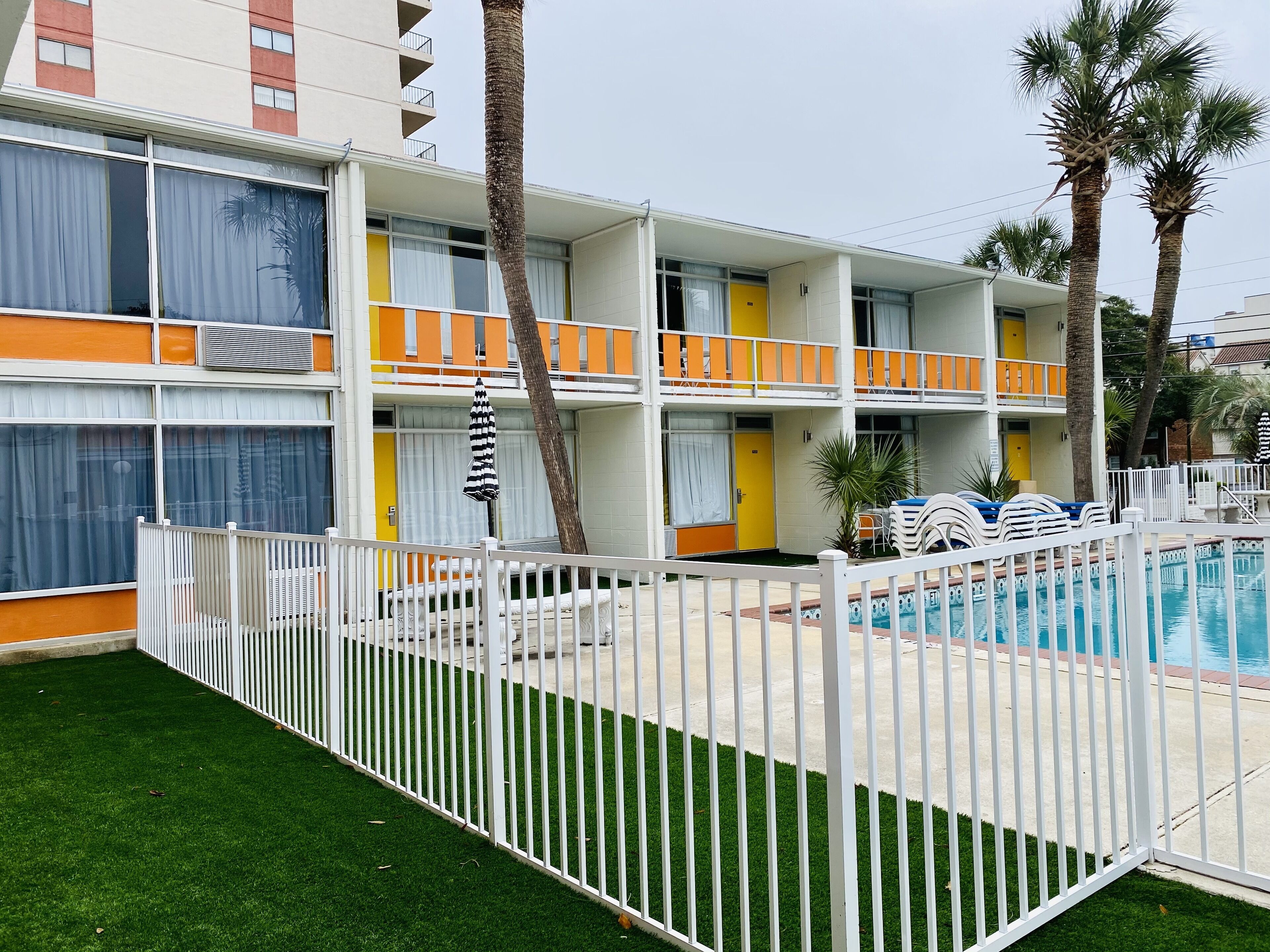 A multi-story hotel with balconies, a swimming pool, and palm trees.