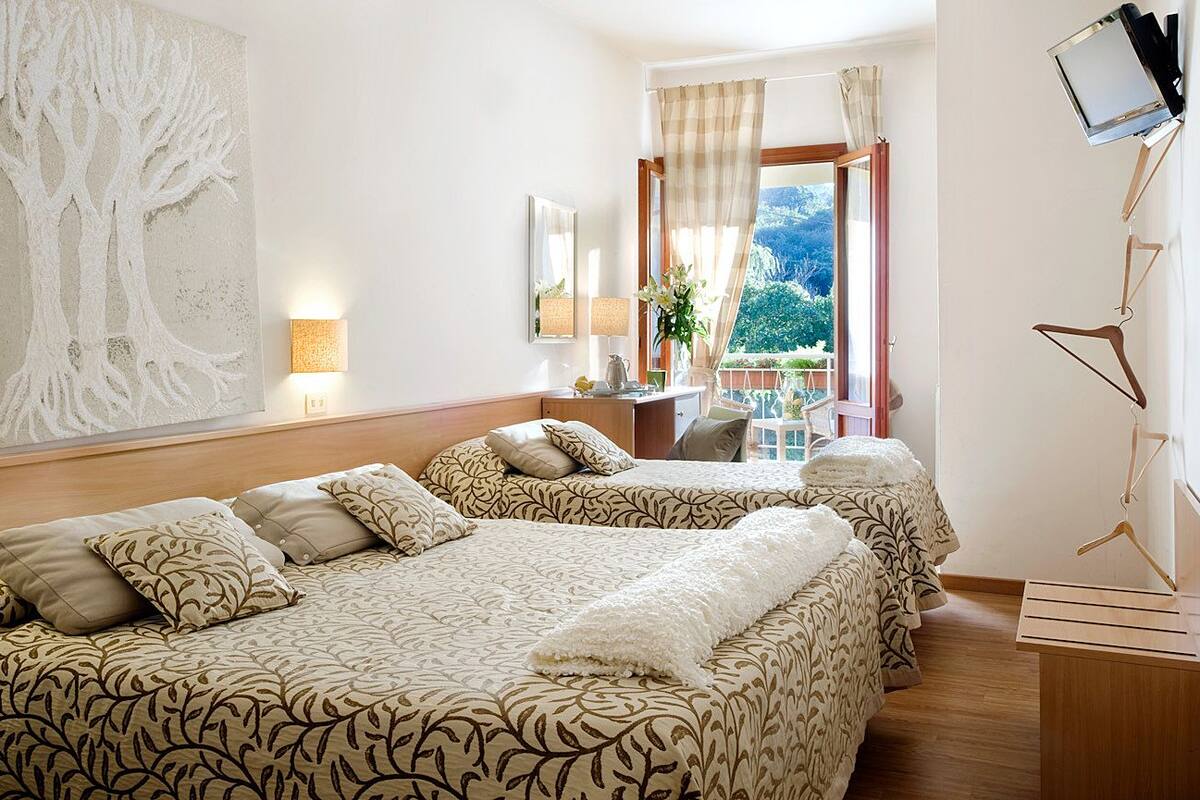 A hotel room with two beds, a desk, a chair, a TV, and a large window with curtains.