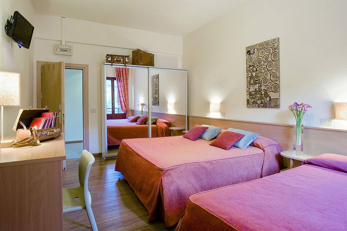 A hotel room with two beds, a desk with a lamp, a chair, a TV, and a wardrobe.