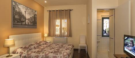 Quarto com cama, mesa de cabeceira, televisão e janela com cortinas.