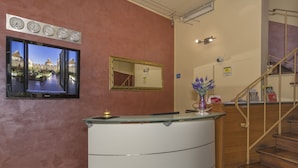 Zona de recepción con un mostrador de vidrio, un reloj en la pared, un espejo y una escalera.
