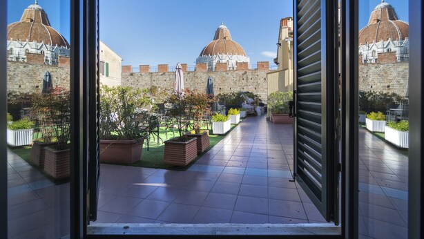 Un patio con suelo de baldosas, plantas en macetas y vistas a un edificio histórico de techos abovedados.