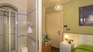 Un baño con ducha, inodoro y perchero para toallas. Hay una mesita de noche con una lámpara y un teléfono.